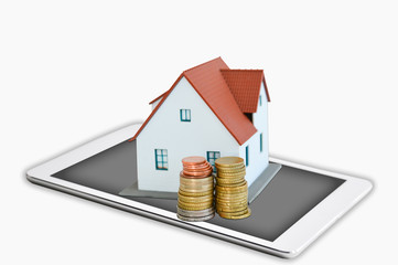 Digital tablet with house model and stack of coins