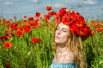Naklejka premium Young beautiful happy girl with long hair in a white dress in the poppy field with a wreath on his head