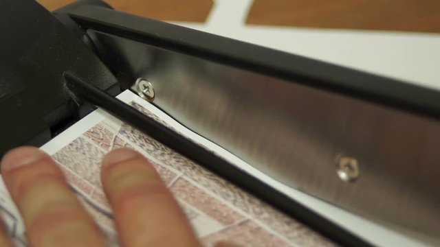 Close up macro shot of an anonymous person using a paper cutter guillotine to trim a printed picture.