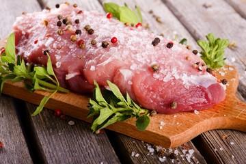 Piece of raw pork meat with salt and pepper on wooden board with herbs