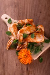 Three marinated chicken wings with oregano and dill on chopping board