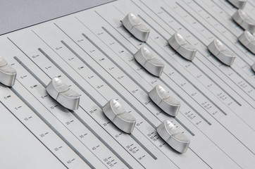 side view closeup of chrome slider buttons forming a wave curve on metallic surface of a sound mixer