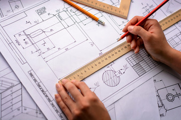 Girl architect draws a plan, graph, design, geometric shapes by pencil on large sheet of paper at office desk. Soft focus