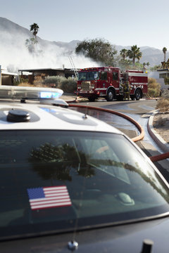 Police car and fire engine parked on road outside the burning house