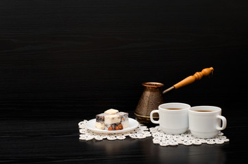 Rahat lokum and two cups of coffee on white napkins, pots on a black background. Space for text
