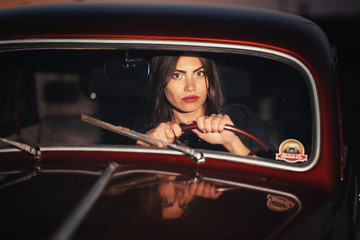 Fototapeta na wymiar beautiful brunette girl with big brightly painted red lipstick lips and in a short dress on high heels next to a retro car on a rural road at sunset
