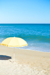 Yellow parasol on desert ocean beach over blue sky