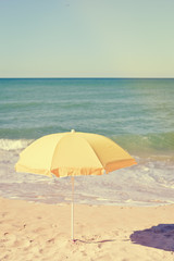 Obraz na płótnie Canvas Yellow parasol on desert ocean beach over blue sky