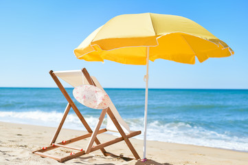 Back View Of Sun Parasol, Woman's Hat and Deckchair On Sandy Beach 