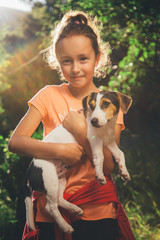 girl holding a small dog breed Jack Russell Terrier smiles and looks at the camera on a summer day