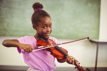 Portrait of smiling schoolgirl playing violin in classroom
