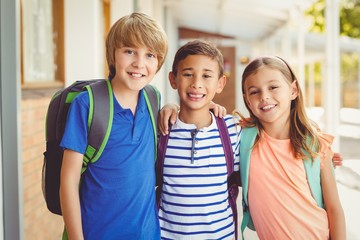 Smiling school kids standing in school corridor with arm around