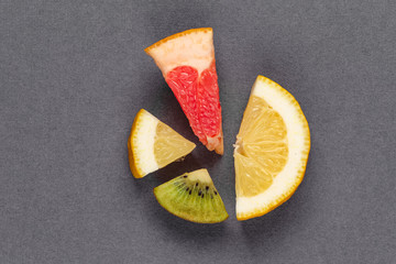 Pie chart of ripe fruit on a gray background. Vitamin fruits: kiwi, grapefruit, lemon. Fruit as a percentage. Template for the poster of summer fruit menu.