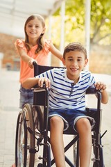 Happy schoolgirl pushing a boy on wheelchair