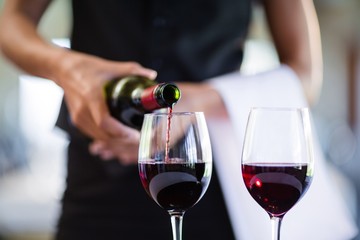 Mid section of waitress pouring red wine in a glass