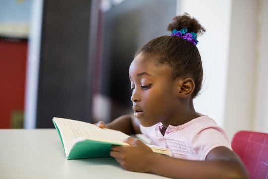 School girl reading book in classroom
