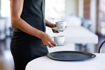 Mid section of waitress serving cup of coffee