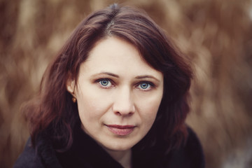 Closeup portrait of beautiful middle age white caucasian brunette woman with green eyes in coat jacket on fall autumn day outside looking in camera on yellow rye background