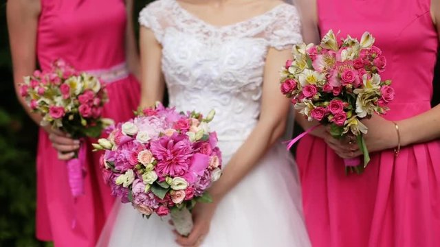 Beautiful bride standing between bridesmaids in pink dresses holding bouquets of roses