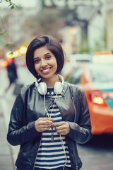 Portrait of beautiful Hispanic latin girl woman short black hair in leather jacket with headphones outside in evening night city street smiling laughing looking in camera, lifestyle portrait concept