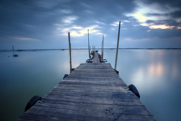 A wooden jetty at lake with blue hour sunset scenery in the background, Soft Focus due to Long Exposure Shot.
