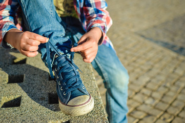 Algarve, Portugal - March 17, 2016: Closeup on kid hands tying laces ready for sport, school fun. sunny background outside 
