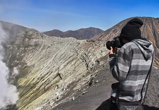 A young traveler try to take photograph at crater of Bromo vocalno, East Java, Indonesia. Photographer take a photo at the crater of volcano.