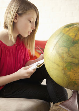 A girl writing in a notepad while sitting next to a world globe