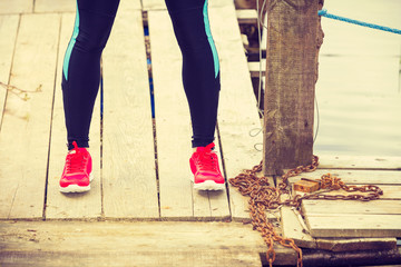 Slim fit legs wearing red sport shoes on wooden pier