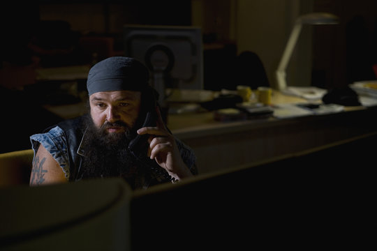 A biker sitting in a darkened office on the phone