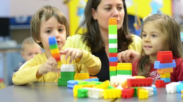 Kids and educator playing with plastic building blocks at kindergarten
