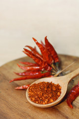 chili powder on wooden spoon and red hot dry chili peppers on background.