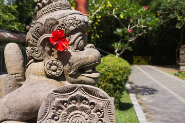 Mythische Steinfigur mit roter Blume auf Bali