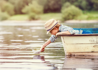 Little boy launch paper ship from old boat on the lake