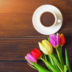 Fototapeta na wymiar A cup of coffee, a bouquet of tulips on a dark wooden table