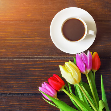 A cup of coffee, a bouquet of  tulips on a dark wooden table