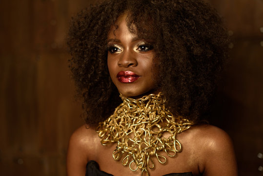 Portrait of beautiful South African young woman with bright red lips wearing gold necklace over bronze wall