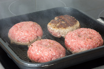raw burgers, beef in a frying pan on cooking surface in kitchen
