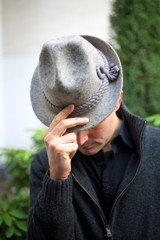 Man holding two fingers and thumb on grey hat while holding his head down, bowing. Concept shot for 'Saying thank you to the audience'.