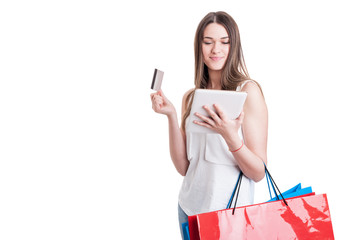 Attractive young shopaholic looking on digital tablet and carryi