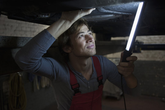 Mechanic holding illuminated fluorescent light while examining car