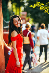 Beautiful brunette girl in red dress with long healthy hair posing on the street