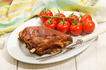 crispy marinated ribs and fresh tomatoes on an oval plate