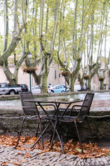 Tables and chairs of street cafes in the town square Luberon among the plane trees in the rain fall.