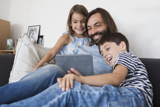 Happy father with children using digital tablet on sofa at home