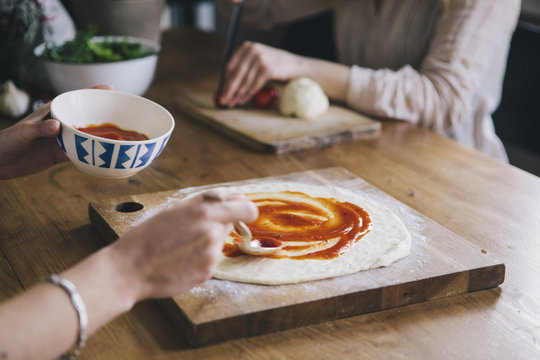Cropped image of woman spreading tomato sauce over pizza dough