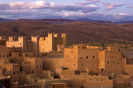 Kasbahs (fortified houses) bathed in evening sunlight with the Jbel Sarhro Mountains in the distance, Nkob, southern Morocco, Morocco