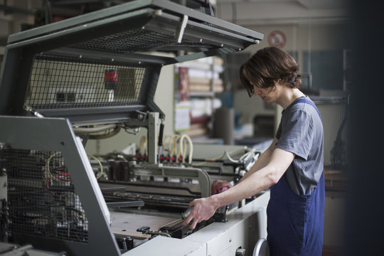 Side view of young manual worker oiling machine in factory