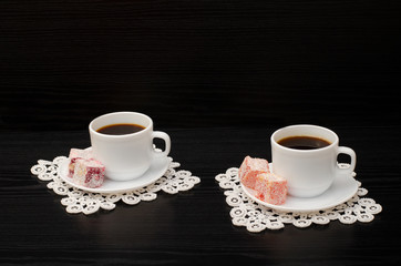 Two cups of coffee on the lace napkins and  turkish dessert on a black background