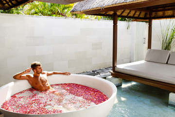 Man Relaxing In Spa Bath. Beautiful Handsome Healthy Male With Sexy Body Bathing, Bathe In Tropical Flower Petals Outdoor Tub, Enjoying Summer Aroma Therapy Beauty Treatment In Day Spa Salon. Relax